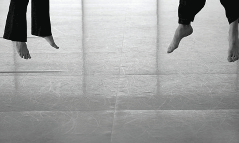 two pairs of feet in black trouser jump off the ground