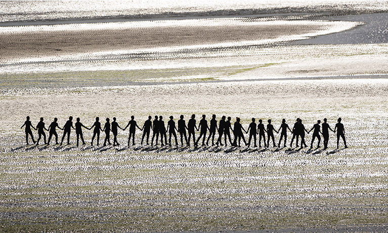 a line of people hold hands on a beach