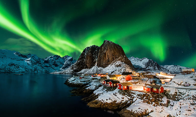 A mountain with the lights of the aurora borealis behind it