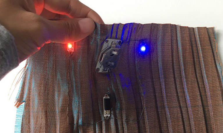 a hand holds fabric with a zip and lights emitting from it