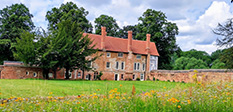 Manor house set back in a field with wild flowers and over shadowing trees