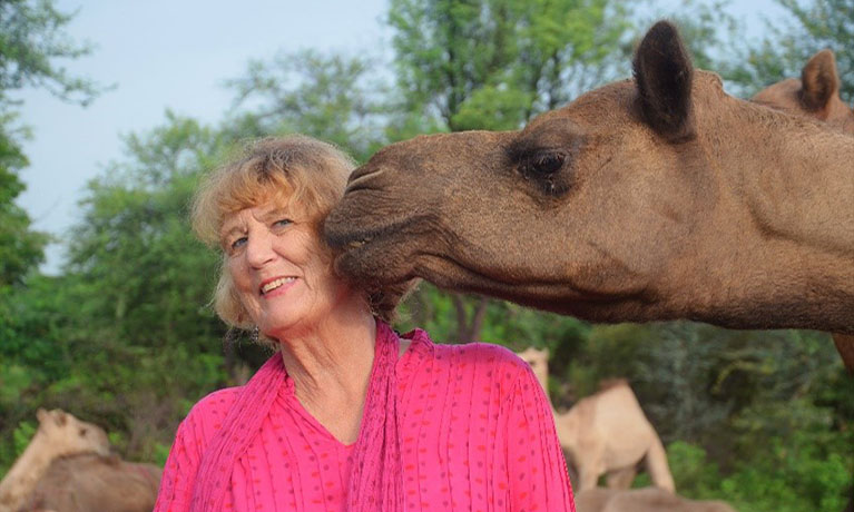Woman with a camel touching its nose to her face