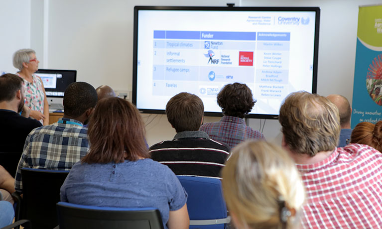 Students in a classroom looking at a screen showing a presentation slide.