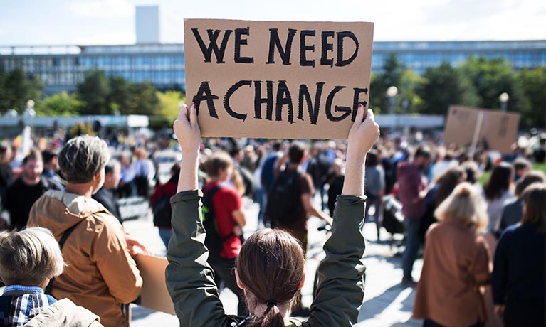 Protester holding up a placard with "we need a change" written on it.