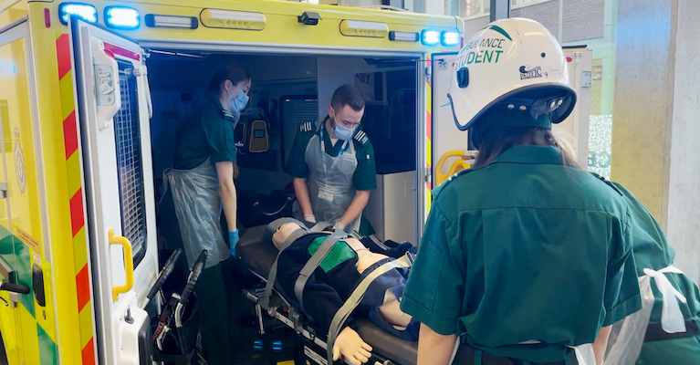Paramedic students wearing protective equipment treating a mock casualty in a simulated ambulance