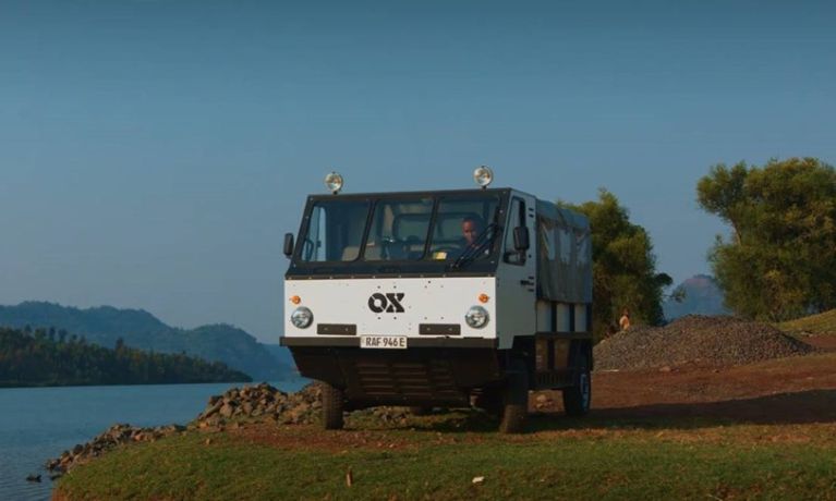 A white truck with OX Delivers branding driving on a dirt track next to a river.