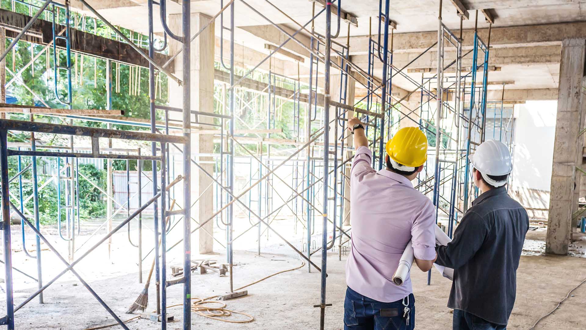 Two males wearing hard hats pointing at scaffolding