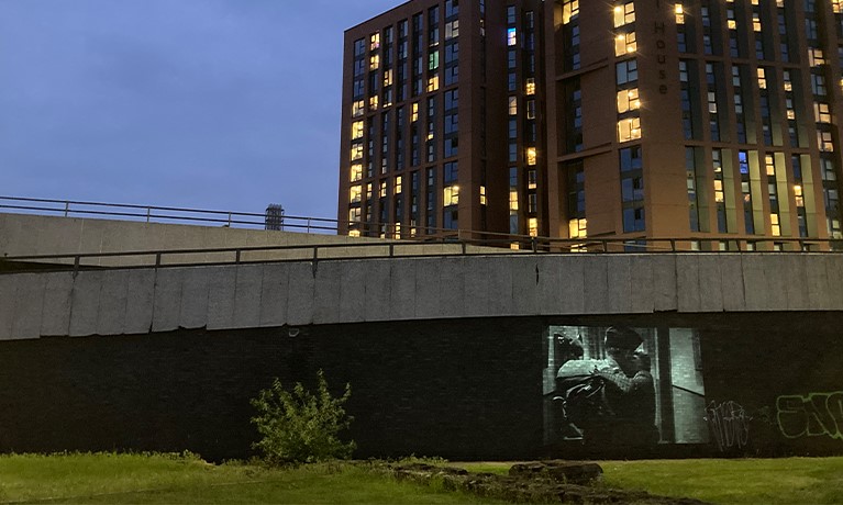 Grafitti on a bridge behind a building in a city at nighttime.