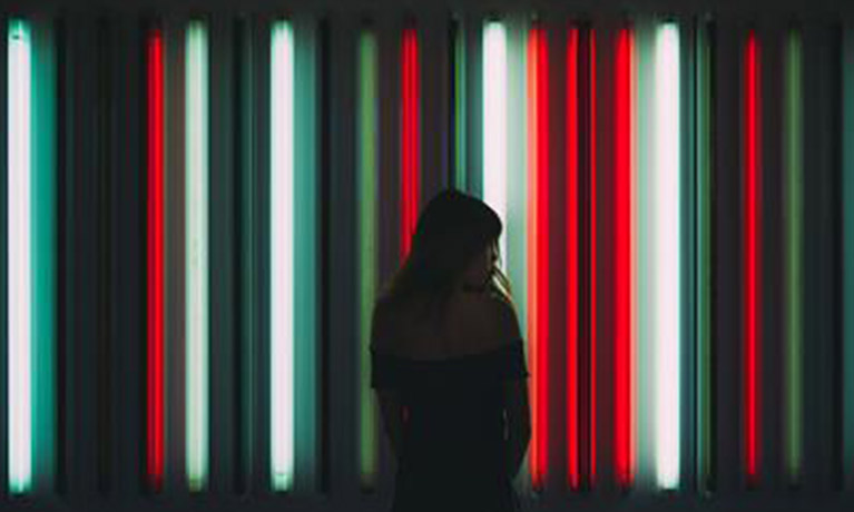 A woman stands in silhouette in front of vertical green, white and red neon lights.