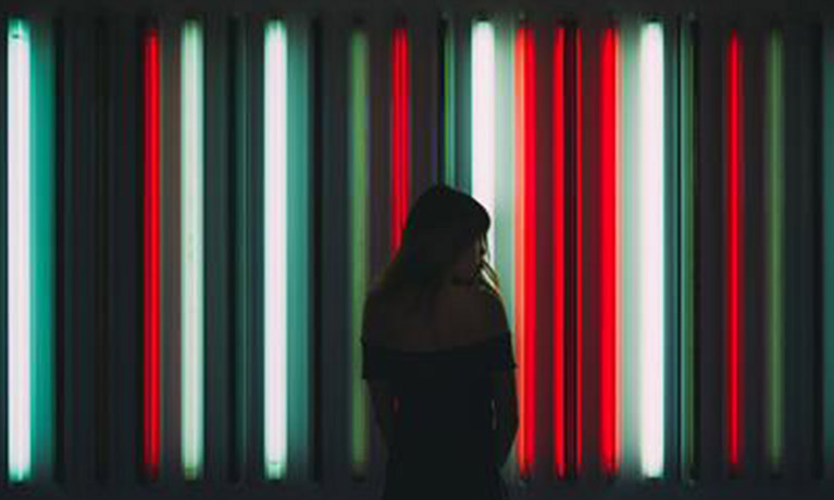 the silhouette of a woman stands in front of vertical neon lights