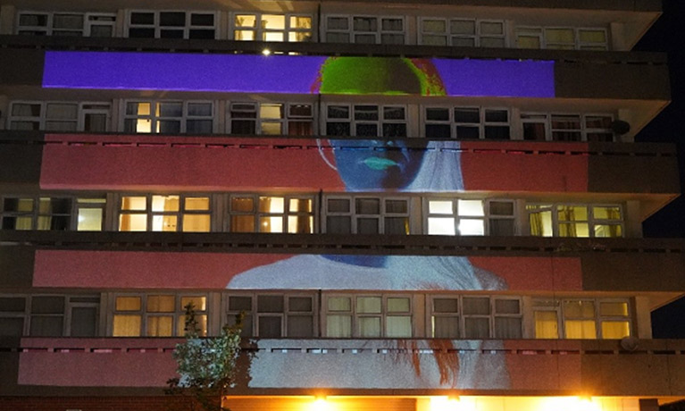 A negative of a woman projected onto a block of flats