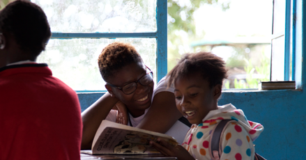 Petra smiling and talking to a young student who is reading a book