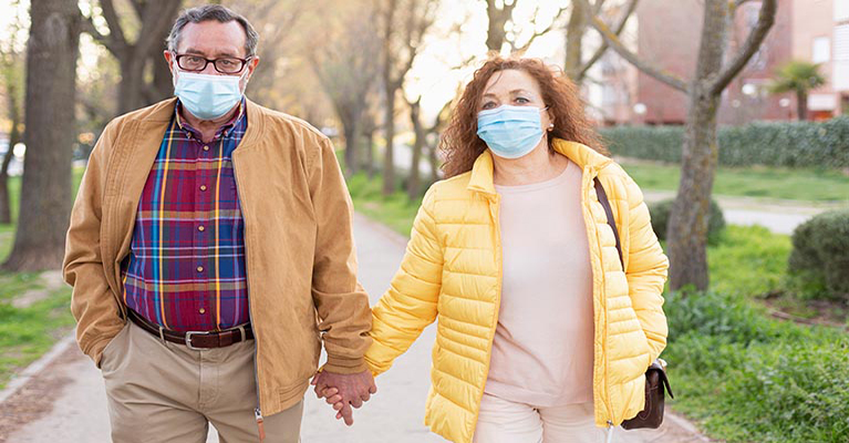 man and woman wearing face masks, holding hands, walking down the street