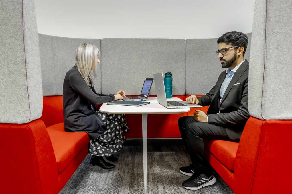 Woman and man sat opposite one another in flexible working pod with laptops