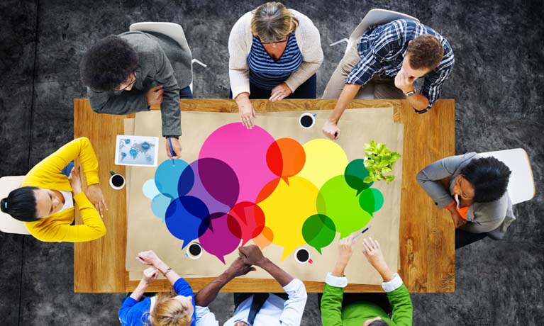 eight adults sat around wooden table with abstract multi-colour speech bubbles