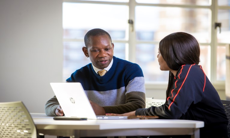 Male and female sat at desk with laptop having a discussion in education setting