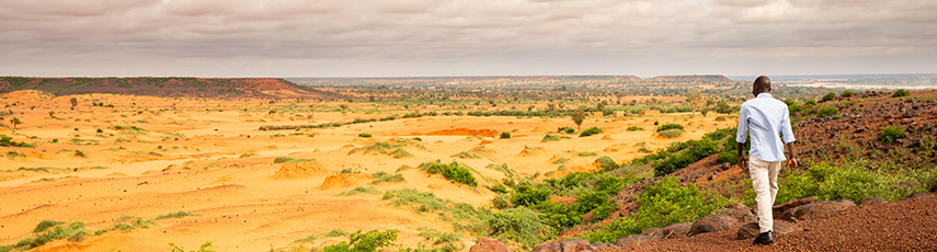 African man taking a walk on stony slopes and sand dunes in the Sahel