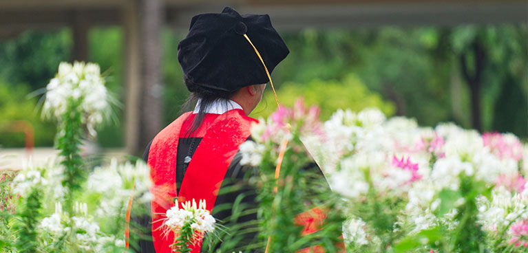 a student in a PhD graduation gown in a field