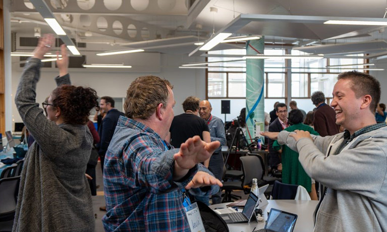 Two men and a woman dance in an office environment smiling.