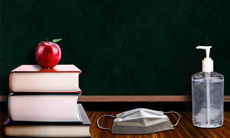 Desk with book, apple, mask and hand sanitiser.