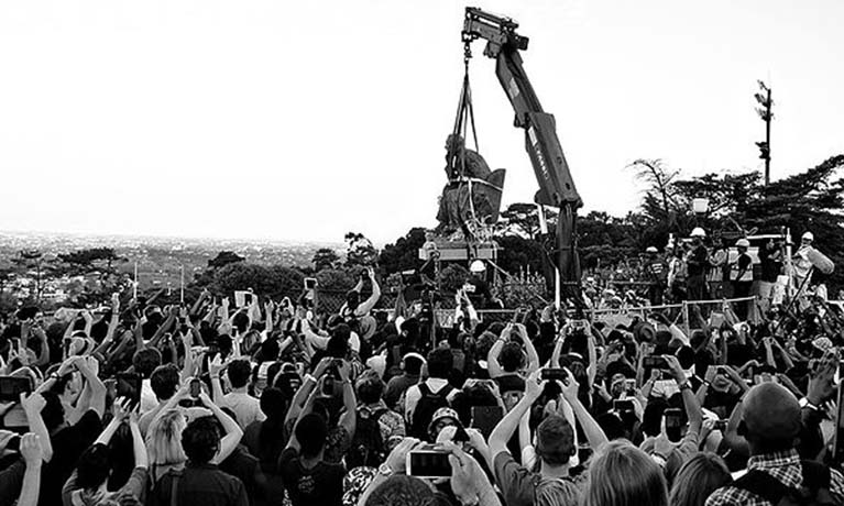 Group of people taking photograph of a statue moving on a crane.