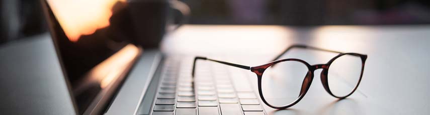 A home office desk with a laptop and eyeglasses.