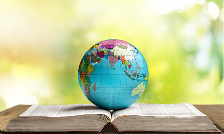 Mini globe placed on open book with outdoor background