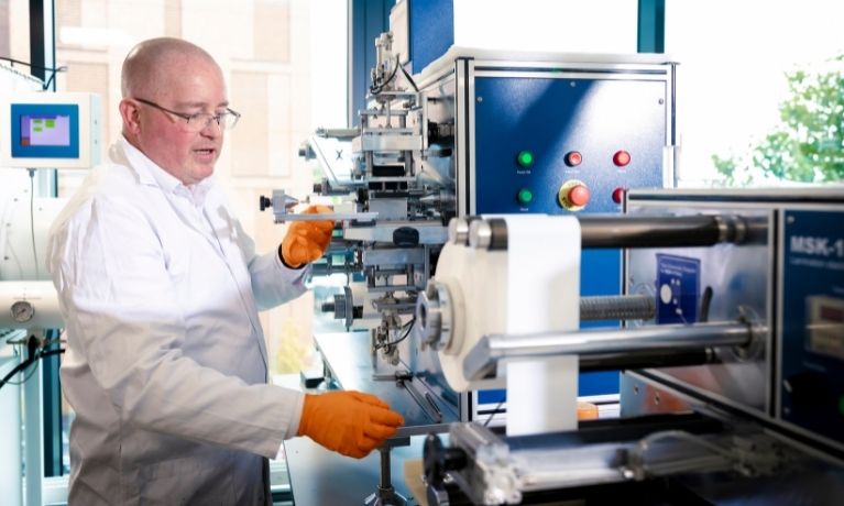A scientist in a white lab coat and orange gloves using a blue cell prototyping machinectronic cable in orange gloves A scientist in a white lab coat and orange gloves using a blue cell prototyping machinectronic cable in orange gloves
