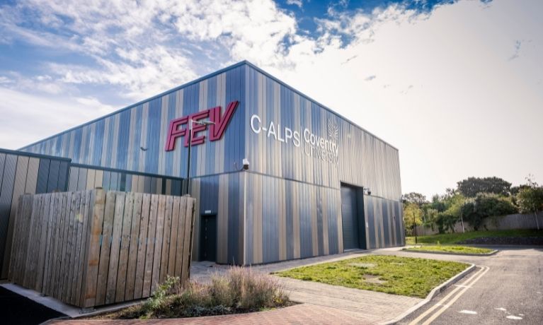 Photo of the grey C-ALPS building on a sunny day with blue sky. There is a large FEV logo in red on the left side of the building