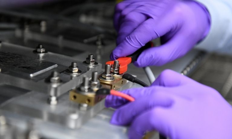 close up of a pair of hands in bright purple gloves twisting dials in a lab setting
