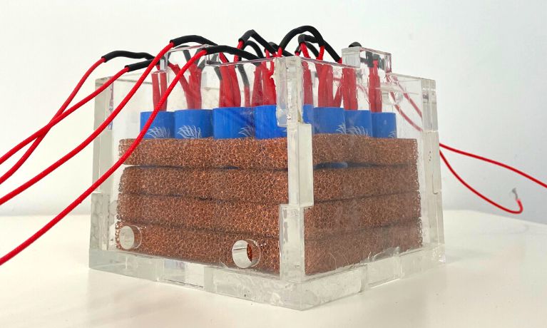 A close up of a Perspex box with 4 layers of copper coil, blue batteries and red cables