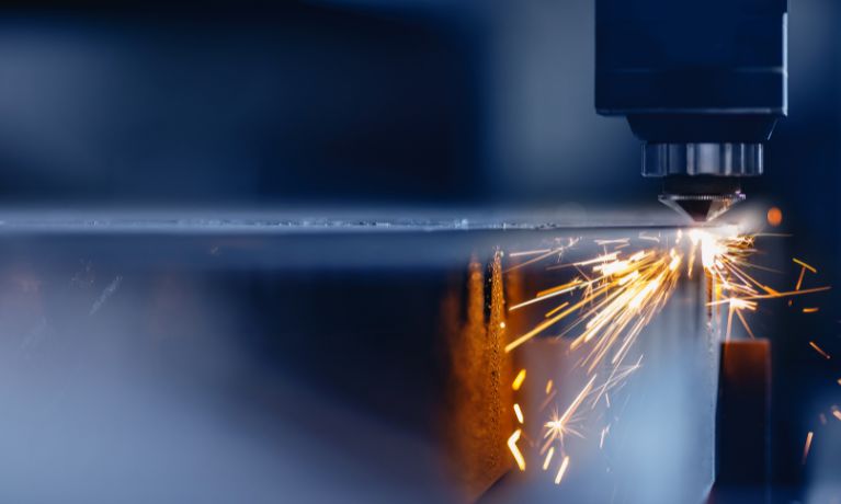 close up of a laser cutting machine with bright orange sparks flying off it