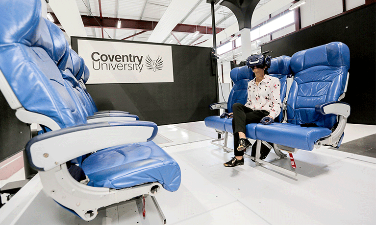 A woman sits on blue airplane style seats wearing a black VR headset A woman sits on blue airplane style seats wearing a black VR headset