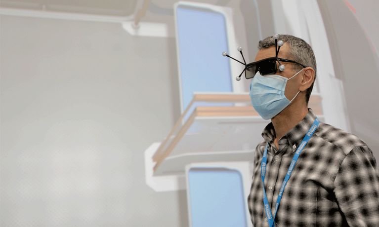 A man in a check shirt with a blue PPE mask wears black glasses with sensors extending from them A man in a check shirt with a blue PPE mask wears black glasses with sensors extending from them