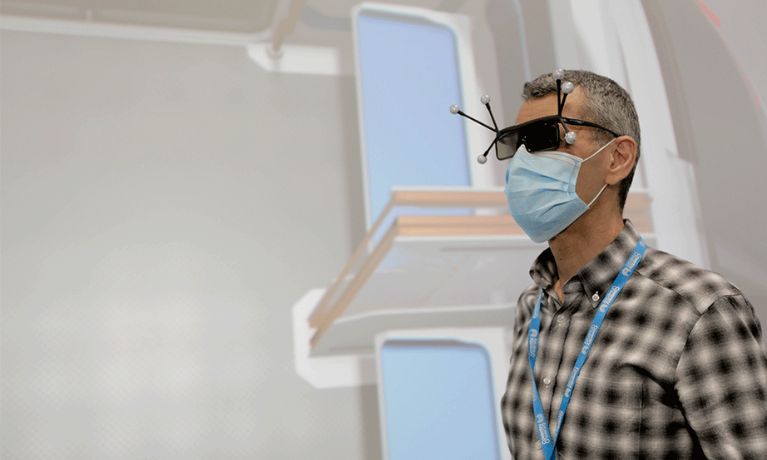A man in a check shirt with a blue PPE mask wears black glasses with sensors extending from them