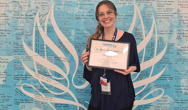 Angelika Berg holding an award with the Coventry phoenix logo in the background