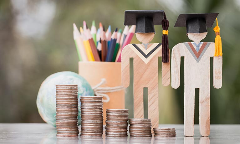 wooden cut outs of graduates wearing graduate hats with piles of wooden coins in front of cut outs