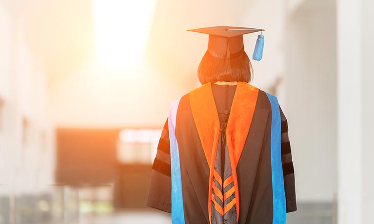 Student in cap and gown walking down corridor.