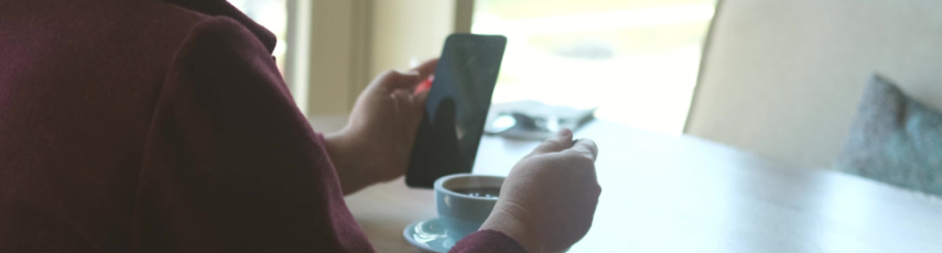 A middle-aged woman with glasses is having lunch in a cafe and reading the news on her smartphone