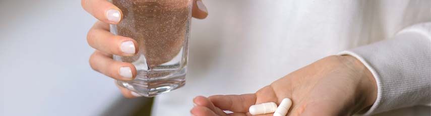 A woman holds a glass of water and two pills in her hands