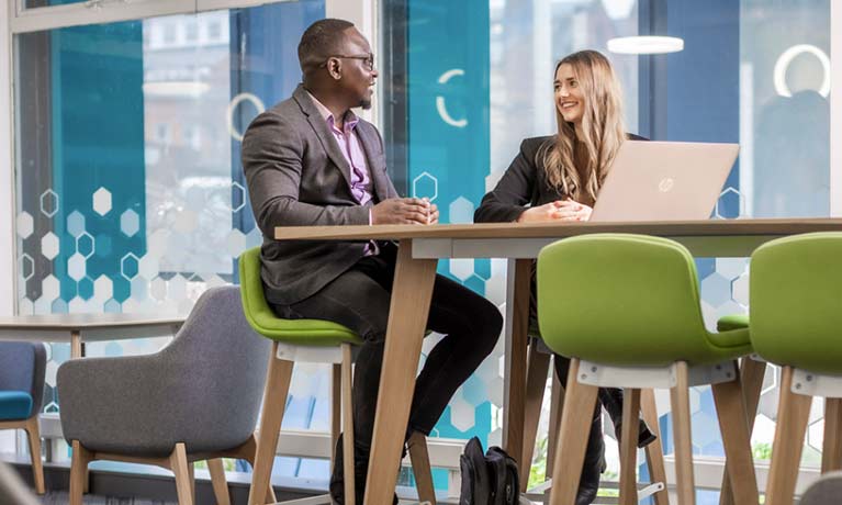 male and female colleagues sitting talking in front of a laptop