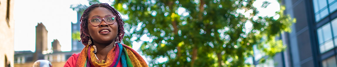 Female student stood in front of trees smiling at camera, outside Coventry University campus.