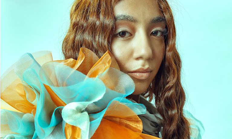 Close up shot of model with curled hair and ruffled orange and blue shoulder