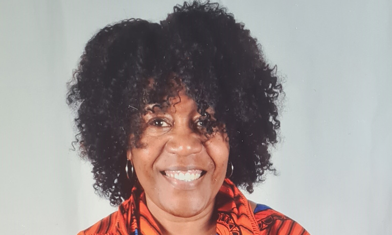 Dr Maxine Pryce-Miller, wearing a colourful shirt and smiling at the camera.