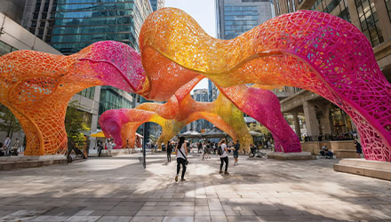 People walking under pink and orange art installation