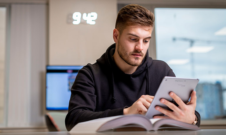 Student sat at a desk reading on his tablet