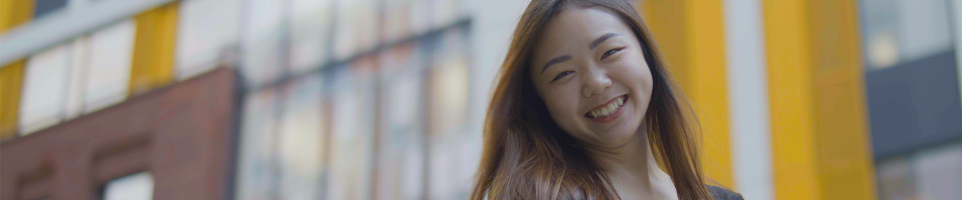 International student stood in front of a modern building smiling at the camera.