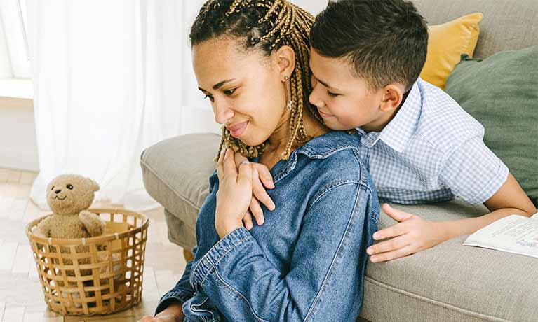 Female looking down at a laptop with her young son hugging her neck