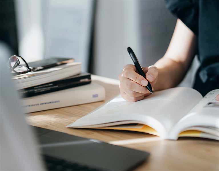 A person writing in a notebook on a desk 