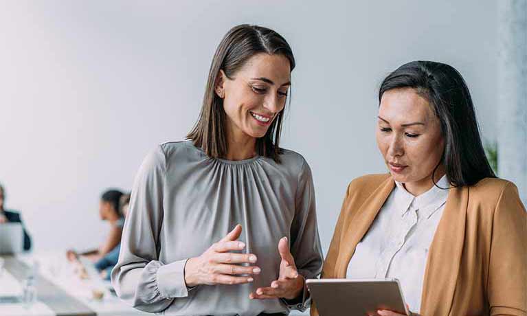 Two females dressed in smart clothes looking at a tablet 
